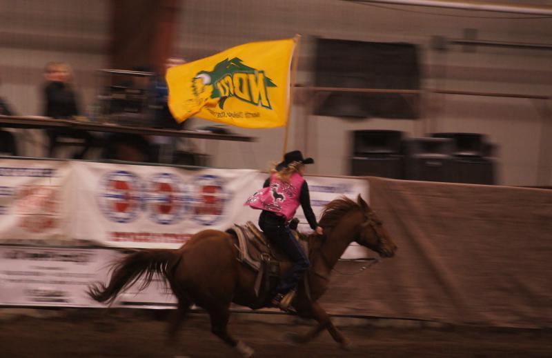 woman riding a horse in a rodeo with a NDSU flag